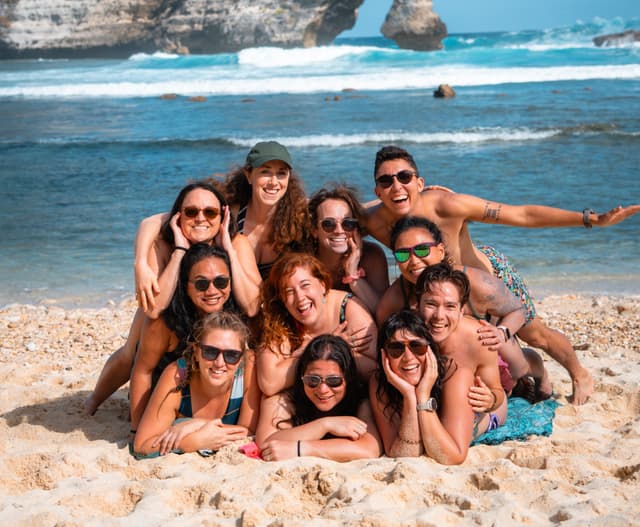 Group of ten happy young friends posing on a sunny sandy beach by the ocean.
