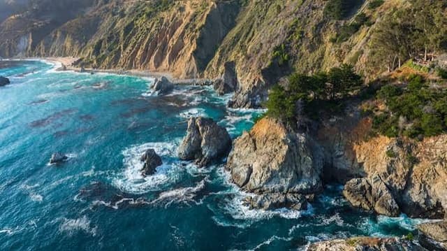 Aerial view of a rugged coastline with turquoise ocean, towering cliffs, and prominent sea stacks.