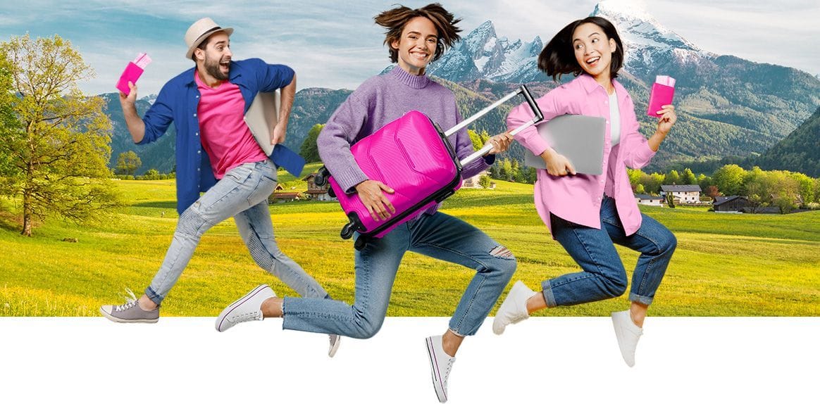 Three joyful travelers jump with a pink suitcase, laptop, and passports in a mountain landscape.