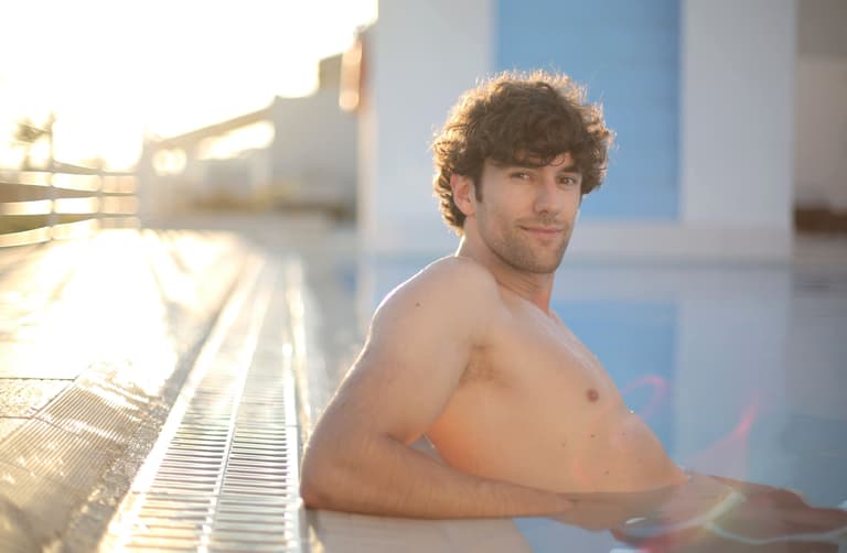 Young man with curly hair enjoying a refreshing swim in a sunlit pool.